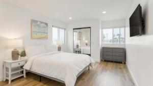 ein weißes Schlafzimmer mit einem Bett und einem Fernseher in der Unterkunft Velvet Sand I by AvantStay Steps to Newport Beach Private Rooftop w Outdoor Kitchen Hot Tub in Newport Beach