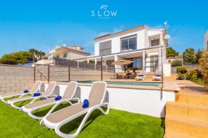 a row of chaise lounges on a lawn near a swimming pool at Villa Es Bufedo by Slow Villas in Cala Pi