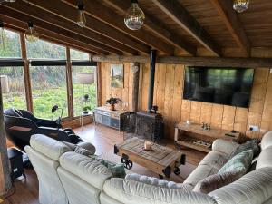 Una sala de estar con sofás blancos y un televisor en una cabaña. en 5 Star Country Retreat, huge Log Cabin over small river, with private hot tub & log burner, WiFi, 65 inch smart TV relax read at Weston Newark, Nottinghamshire, en Weston