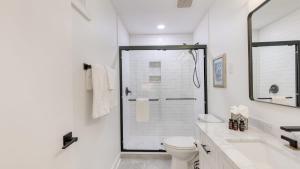 a white bathroom with a shower and a toilet at Conch Cottage by AvantStay Walk to Beach Deck Fireplace Outdoor Dining in Isle of Palms +35 photos