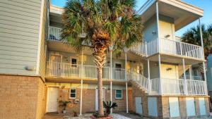 an apartment building with a palm tree in front of it at Sleeps 16 2 Beachfront Condos PoolPickleballTennis Island Retreat Complex in Port Aransas