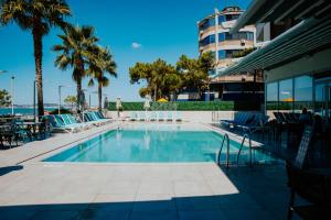 a swimming pool with palm trees and a building at AMR Hotel - Durres in Durrës