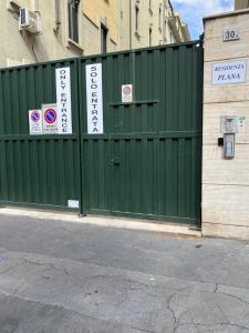 ein grüner Zaun mit Schildern neben einem Gebäude in der Unterkunft Residenza Plana in Mailand