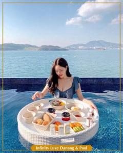 a woman in the water with a tray of food in a pool at Infinity Luxe Danang & Pool in Da Nang