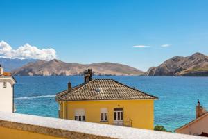 a yellow house with a view of the water and mountains at Studio Apartments Cavrak with Terrace in Baška