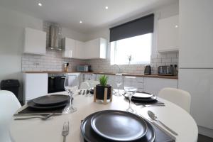a white kitchen with a table with plates and glasses at Signature - Hattrix View in Cumbernauld