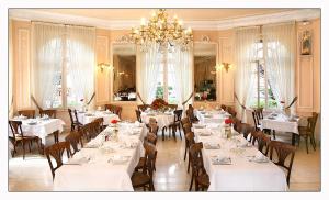 a restaurant with white tables and chairs and a chandelier at Hôtel Métropole in Lourdes