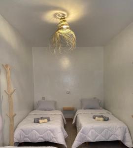 two beds in a room with a chandelier at Titryte Hostel - chill rooftop in Aourir