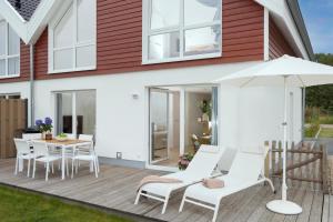 eine Terrasse mit weißen Stühlen und einem Sonnenschirm in der Unterkunft Villa am See für bis zu 6 Personen mit Kaminofen, Badewanne und Sauna - Haustiere herzlich willkommen, direkt am Wasser gelegen in Nordhorn