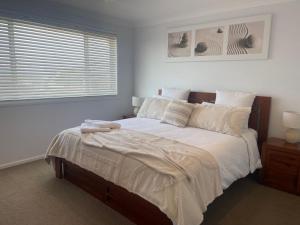 a bedroom with a bed with white sheets and a window at Sandy Adventures - Pet Friendly - 1 MIn to Beach in Callala Beach