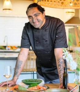 a man with tattoos on his arms standing in a kitchen at The Kina Cottage in Tutukaka
