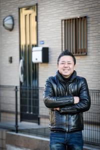 a man in a leather jacket standing in front of a building at J's Backpackers in Tokyo