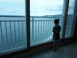 a little girl looking out a window at the water at Ocean Trium 트리움 in Hwaam