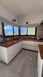 a kitchen with white cabinets and windows with mountains at Sol & Río Refugio Serrano in Villa Las Rosas