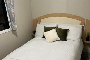 a bed with white sheets and green pillows at 3 Bedroom Caravan - Sleeps 8 - Parking Wifi Pool in Clacton-on-Sea
