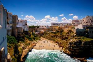 a group of people standing on a beach next to the ocean at La Steila del Sud in Polignano a Mare