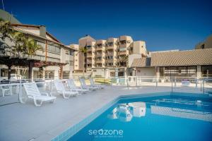 einen Pool mit weißen Stühlen neben einem Gebäude in der Unterkunft Condomínio bem localizado a 100m da Praia - CSC in Florianópolis