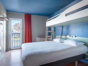 a bedroom with a white bed with a blue wall at ibis budget Caen Hérouville in Hérouville-Saint-Clair