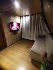 Habitación pequeña con sofá y TV en la pared. en Chalé Ypê Amarelo Ypês da Serra, en Pirenópolis