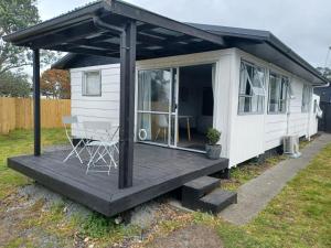 a white tiny house with a porch and a deck at Cosy Cottage in Ruakaka