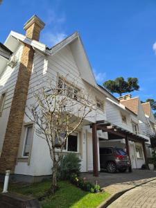 a white house with a car parked in the driveway at Casa 3 suítes no Centro de Canela in Canela