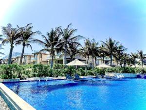 a swimming pool with chairs and umbrellas and palm trees at Villa Beachfront in Cam Lâm
