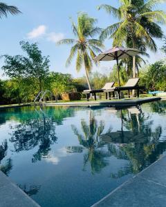 a pool with a table and an umbrella and palm trees at Aaryana Lagoon in Tangalle