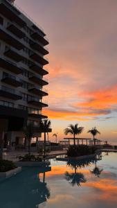 a sunset over a building and a pool with palm trees at Progreso Luxury Oceanfront Condo at Yucalpetén Resort Marina in Progreso