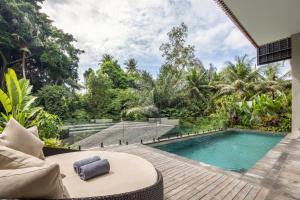 a swimming pool in a garden with a table and a couch at Adiwana Unagi Riverfront in Ubud