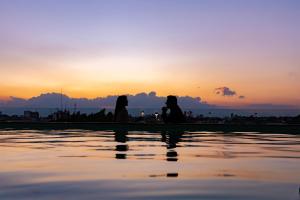 three people sitting on the edge of the water at sunset at Banyan Tree Puebla in Puebla