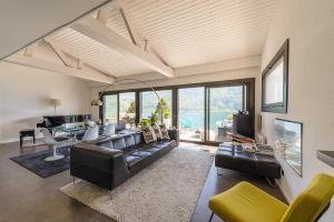 ein Wohnzimmer mit einem schwarzen Ledersofa und Stühlen in der Unterkunft Le Cristal - Prestigieux appartement au Lac d'Annecy in Doussard