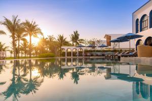 a swimming pool with palm trees and a building at Hoi An Royal Beachfront Resort & Villas in Dien Ban
