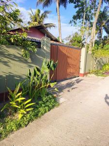 a fence next to a house with palm trees at Sunee'S Home Stay in Ahangama