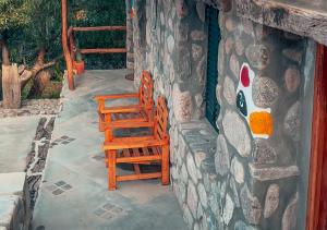 2 sillas de madera sentadas junto a una pared de piedra en La Claudina - Cabañas Boutique en las Sierras, en Capilla del Monte