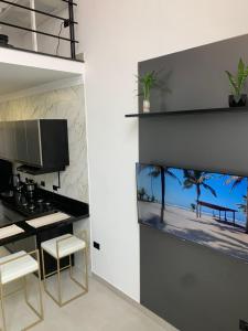 a kitchen with a black counter and white stools at Loft de luxo em Peruíbe, 3 minutos da praia in Peruíbe