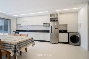 a white kitchen with a table and a refrigerator at Apt w/ balcony and grill 220m from the Sea ALB0201 in Florianópolis