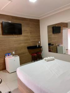a bedroom with a white bed and a flat screen tv at Parati - Hotel Pousada e Motel in Quatá