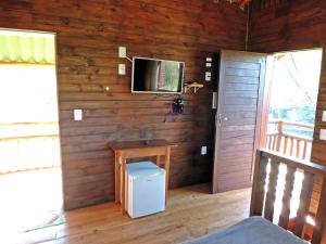 Zimmer mit einer Holzwand, einem TV und einem Tisch in der Unterkunft Pousada Viajantes do Tempo in Cunha
