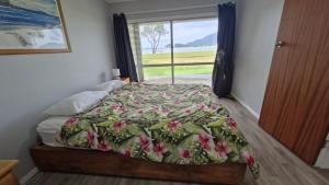 Un dormitorio con una cama con edredón floral y una ventana. en Tairua Harbourside Haven, en Tairua