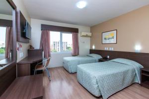 a hotel room with two beds and a desk at Hotel Suárez São Leopoldo in São Leopoldo