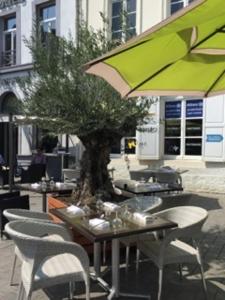 a table and chairs with a tree and a green umbrella at Hotel Restaurant Les Arcades in Valenciennes