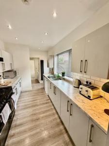 a large kitchen with white cabinets and wooden floors at 5 Bed 2 Shower Home in Stoke on Trent