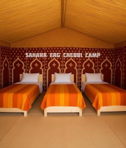 2 camas en una habitación con naranja y blanco en Sahara Erg Chebbi Camp, en Merzouga