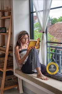 a woman sitting on a window sill reading a book at NEW Cozy, smart, flat above Ubud's roofs - Western Standard in Ubud