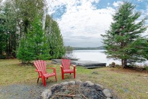 two red chairs and a fire pit next to a lake at Chalet familial forêt & kayak in Nominingue