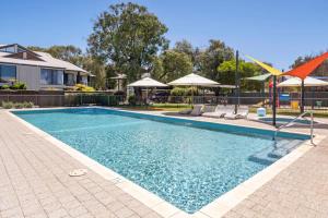 a swimming pool with chairs and umbrellas next to a house at 63CapeView Geographe bay in Broadwater