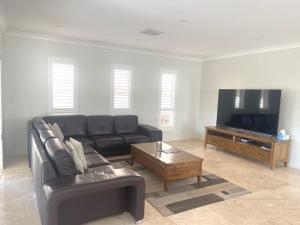 a living room with a leather couch and a flat screen tv at Sunkissed Manor - Swimming Pool - 3 Mins to Beach in Callala Beach