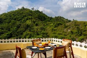 une table et des chaises sur une terrasse avec une montagne dans l'établissement StayVista at Samar Fateh Garh with Bonfire, Lawn, AC, à Rāma