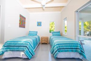 two beds in a room with white walls and windows at Frederick and Ngamata's Beach House in Rarotonga