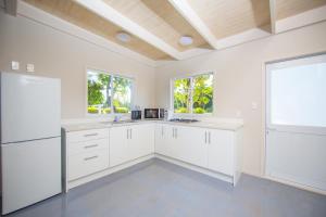 a white kitchen with white cabinets and windows at Frederick and Ngamata's Beach House in Rarotonga
